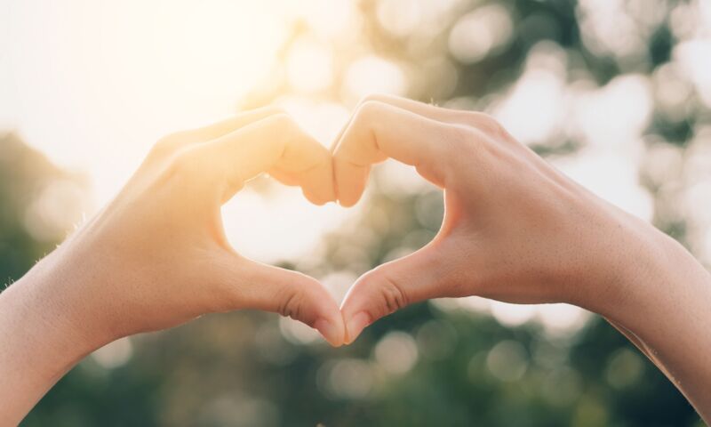 Zwei Hände bilden ein Herz vor hellem Himmel - Symbol für Liebe und Vertrauen