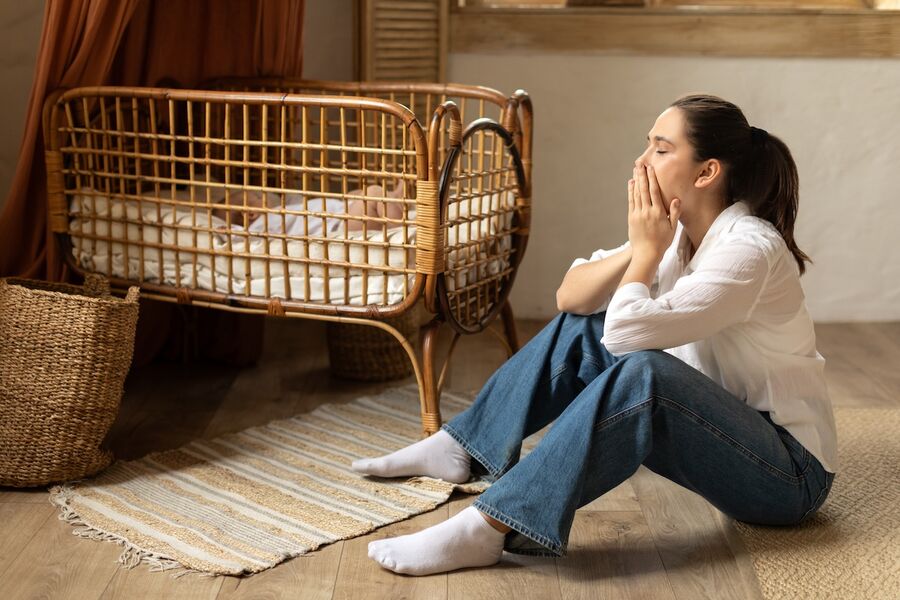 Erschöpfte Mutter mit Wochenbettdepression sitzt neben dem Kinderbett ihres Babys